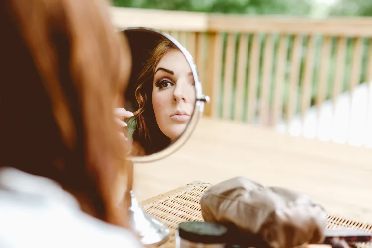 A bride doing her makeup, seen in a round mirror