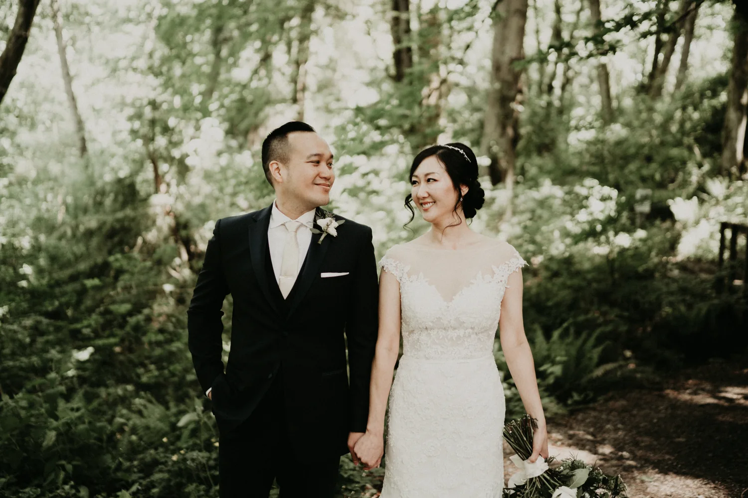 Bride and groom smiling at each other among ferns and tall trees