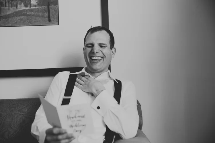 A groom laughing as he reads a card, in black and white
