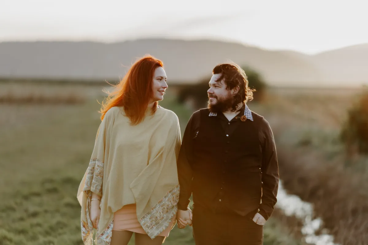 A couple walking hand in hand through a sunlit meadow